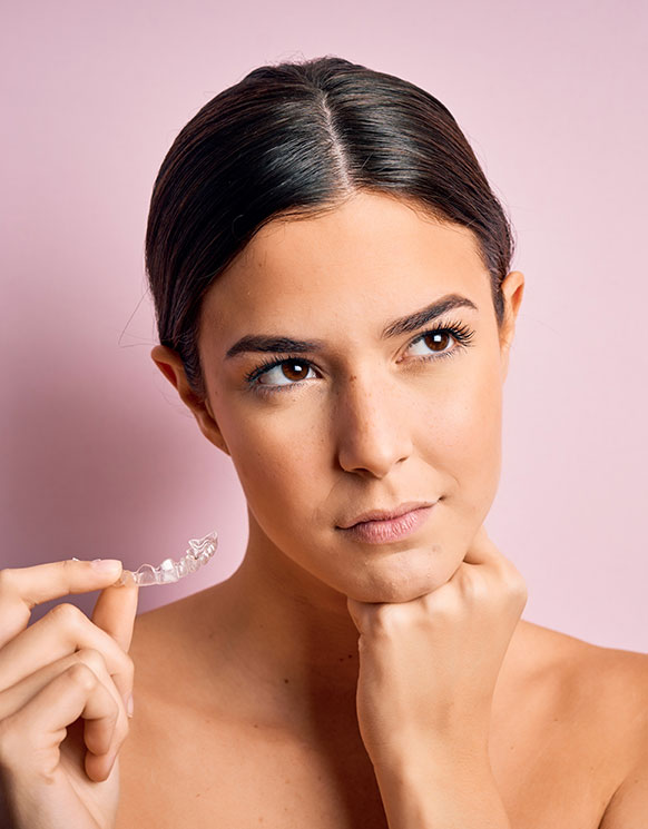 a woman holding invisalign and putting one fist under her chin