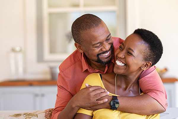 a black couple hugging and smiling with white teeth while looking at each other