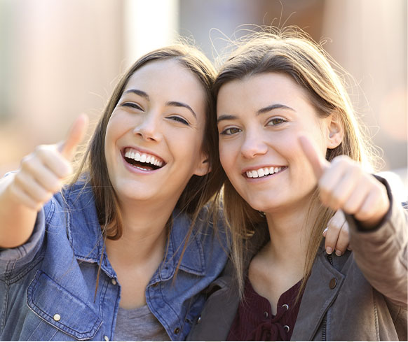 two girls smiling with white straight teeth and showing thumbs up