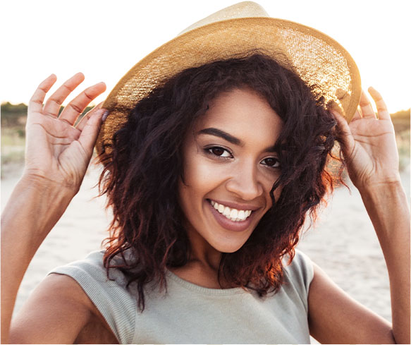 a woman on the beach in a hat smiling