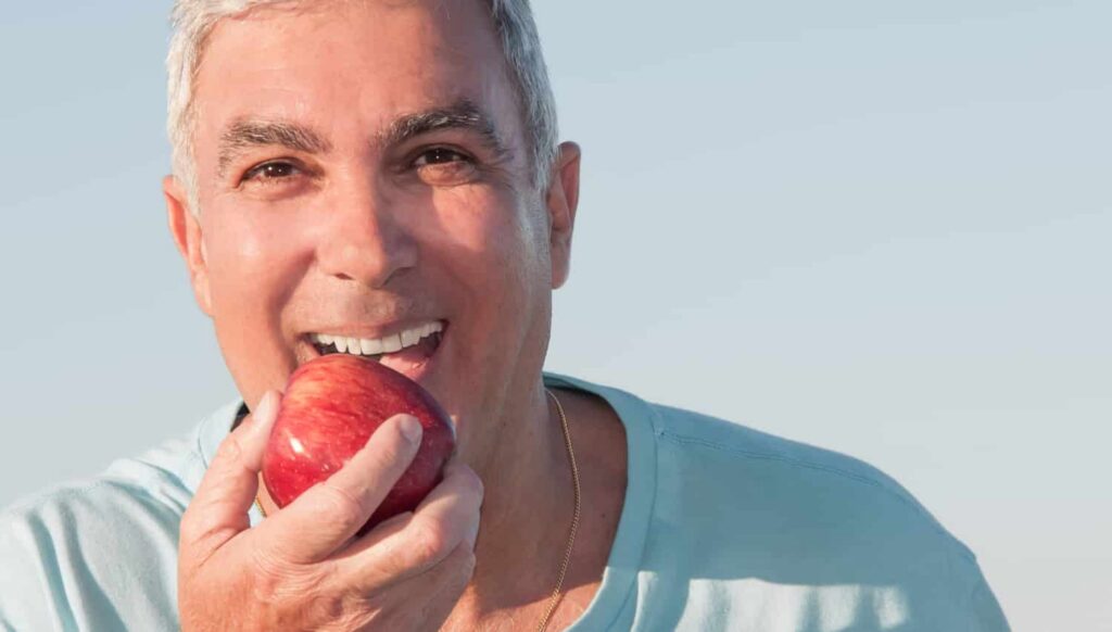 a man with implant supported dentures biting into an apple