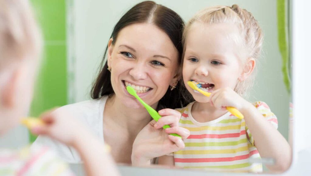 a mother practicing good dental hygiene with her young daughter