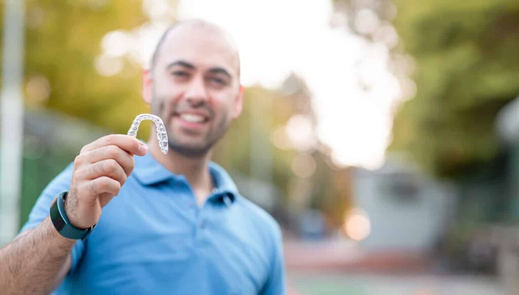 Man holding clear Invisalign aligner outdoors, demonstrating proper care and use of orthodontic treatment for teeth straightening.