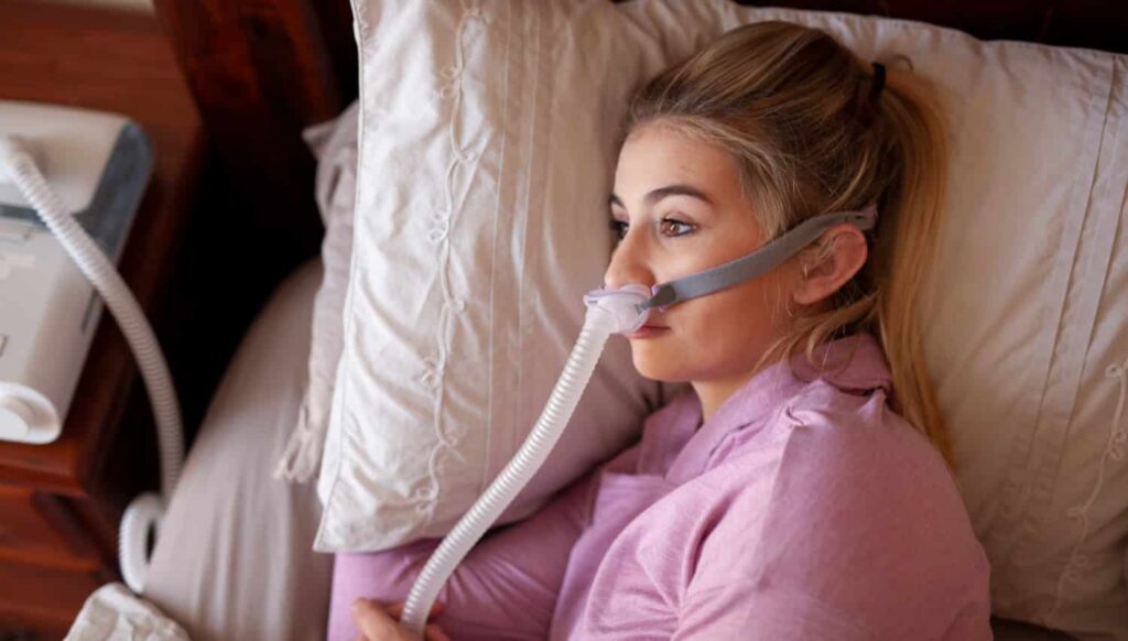 Woman wearing CPAP mask in bed, illustrating common sleep apnea treatment.