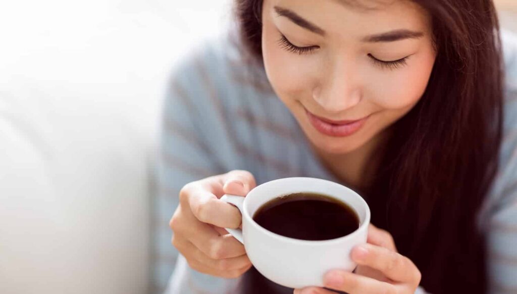 Woman enjoying a cup of coffee, highlighting a common cause of teeth staining and discoloration.
