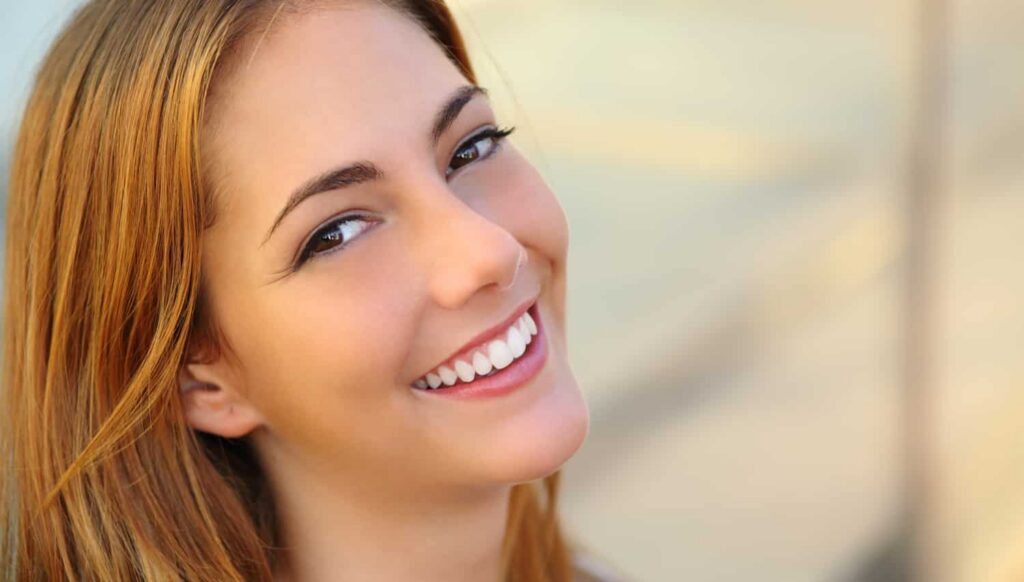 Smiling woman with straight, white teeth showcasing confidence and a healthy smile, relevant to cosmetic dental care and concerns.