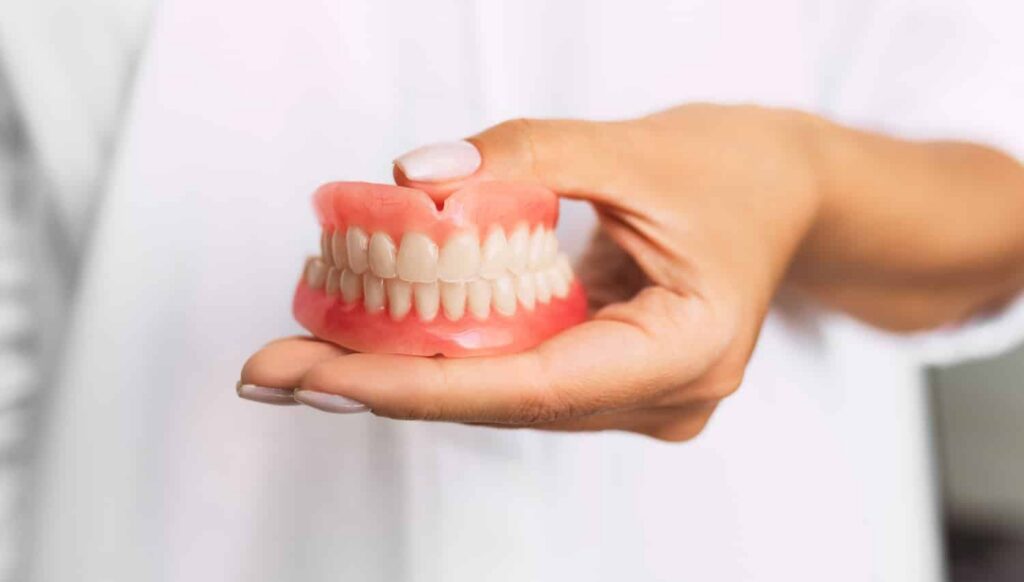 Hand holding a set of dentures, illustrating the topic of when to consider getting dentures and the importance of oral health.