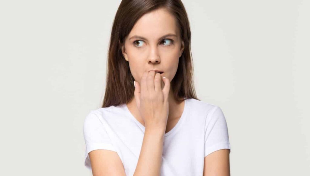 Woman with anxious expression biting her nails, illustrating dental anxiety related to visiting the dentist.