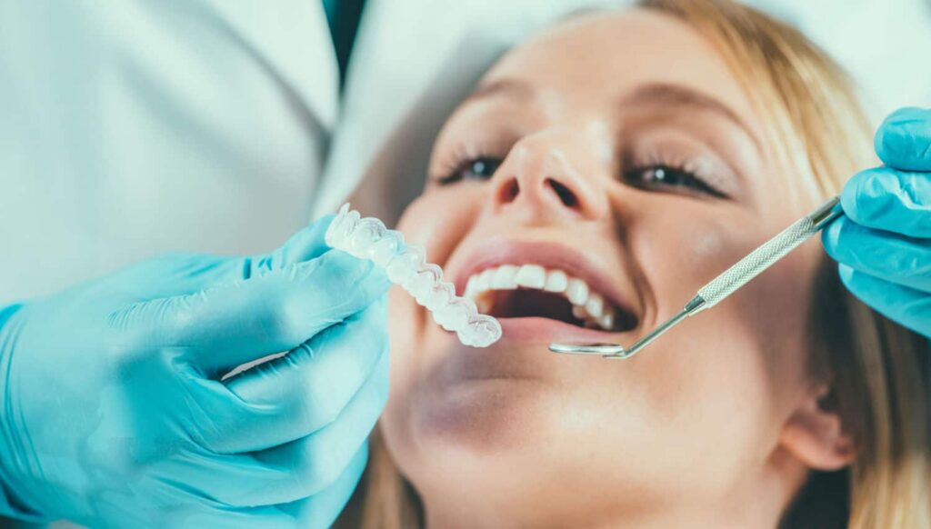 Patient smiling while a dentist in gloves uses a dental tool and a clear aligner, illustrating cosmetic dentistry procedures for smile enhancement.
