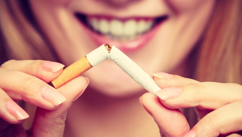 Woman smiling while breaking a cigarette, symbolizing quitting smoking and improving oral health.