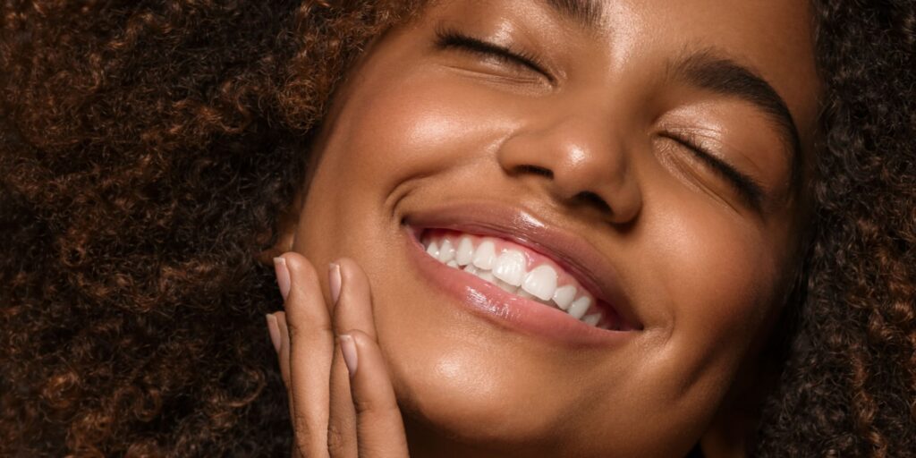 Smiling woman with curly hair showcasing bright, healthy teeth, reflecting the benefits of dental care options like veneers, crowns, and implants.
