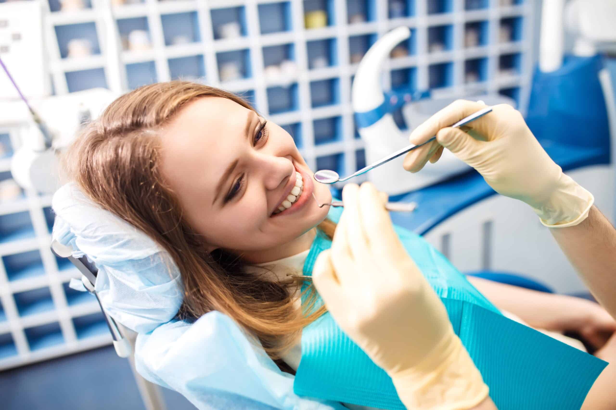 Patient smiling in dental chair during examination, dentist holding dental tools, in a modern dental office setting.