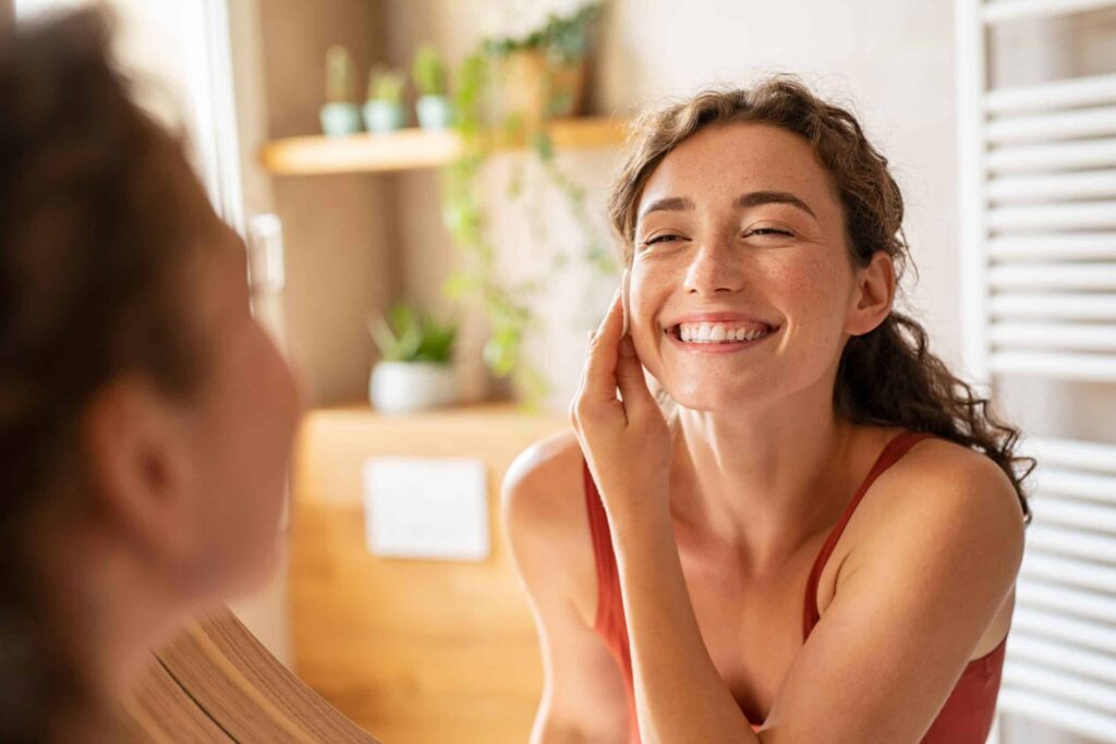 Smiling woman in front of a mirror showcasing a healthy smile, reflecting the connection between oral health and mental well-being.