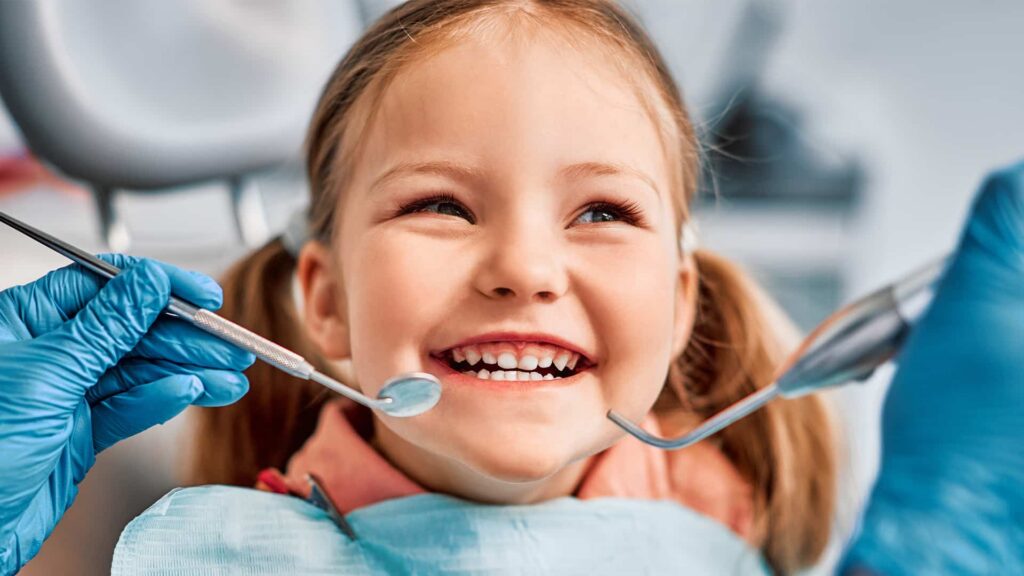 Child smiling during dental check-up, with dentist's tools in view, highlighting modern dental care practices related to global traditions.