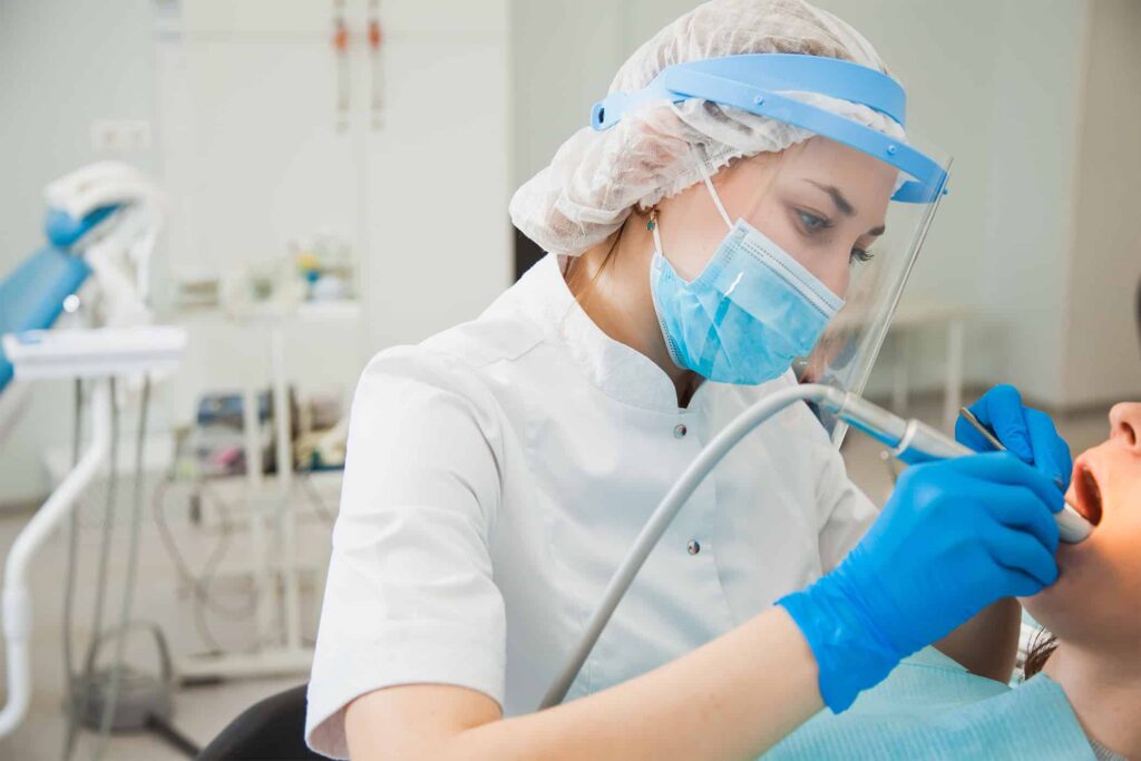 Dental professional wearing protective gear and mask, performing treatment on a patient in a modern dental office, emphasizing a calm and safe environment for addressing dental anxiety.