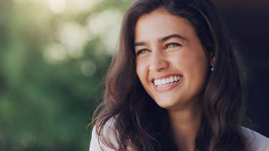 Smiling woman with healthy teeth and long hair, illustrating the connection between aesthetics and oral health in dentistry.