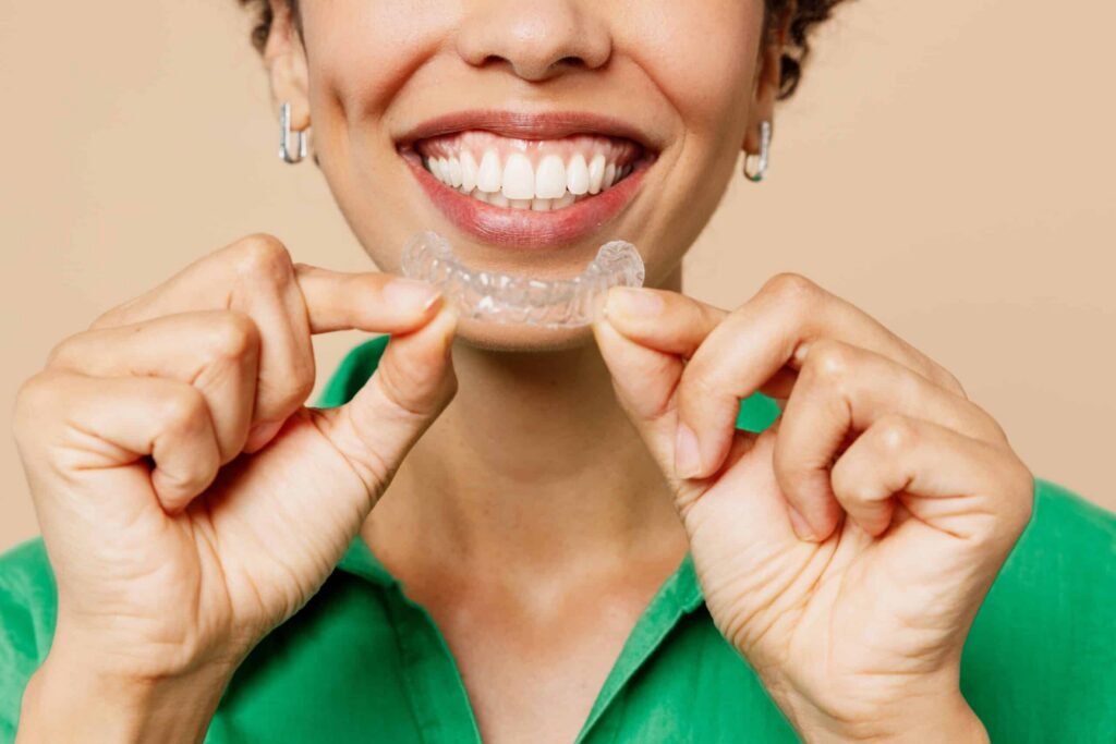 Smiling woman holding clear Invisalign aligner, showcasing discreet teeth-straightening option for adults.