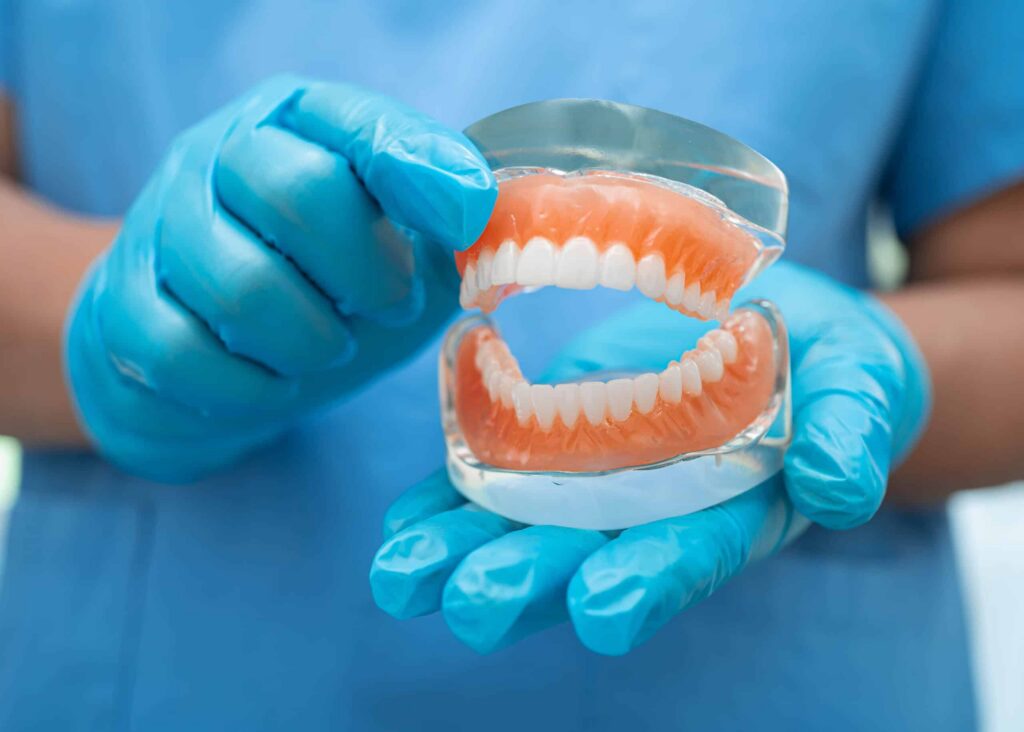 Person wearing blue gloves holding a dental model of dentures, showcasing the upper and lower sets, emphasizing options for tooth replacement.
