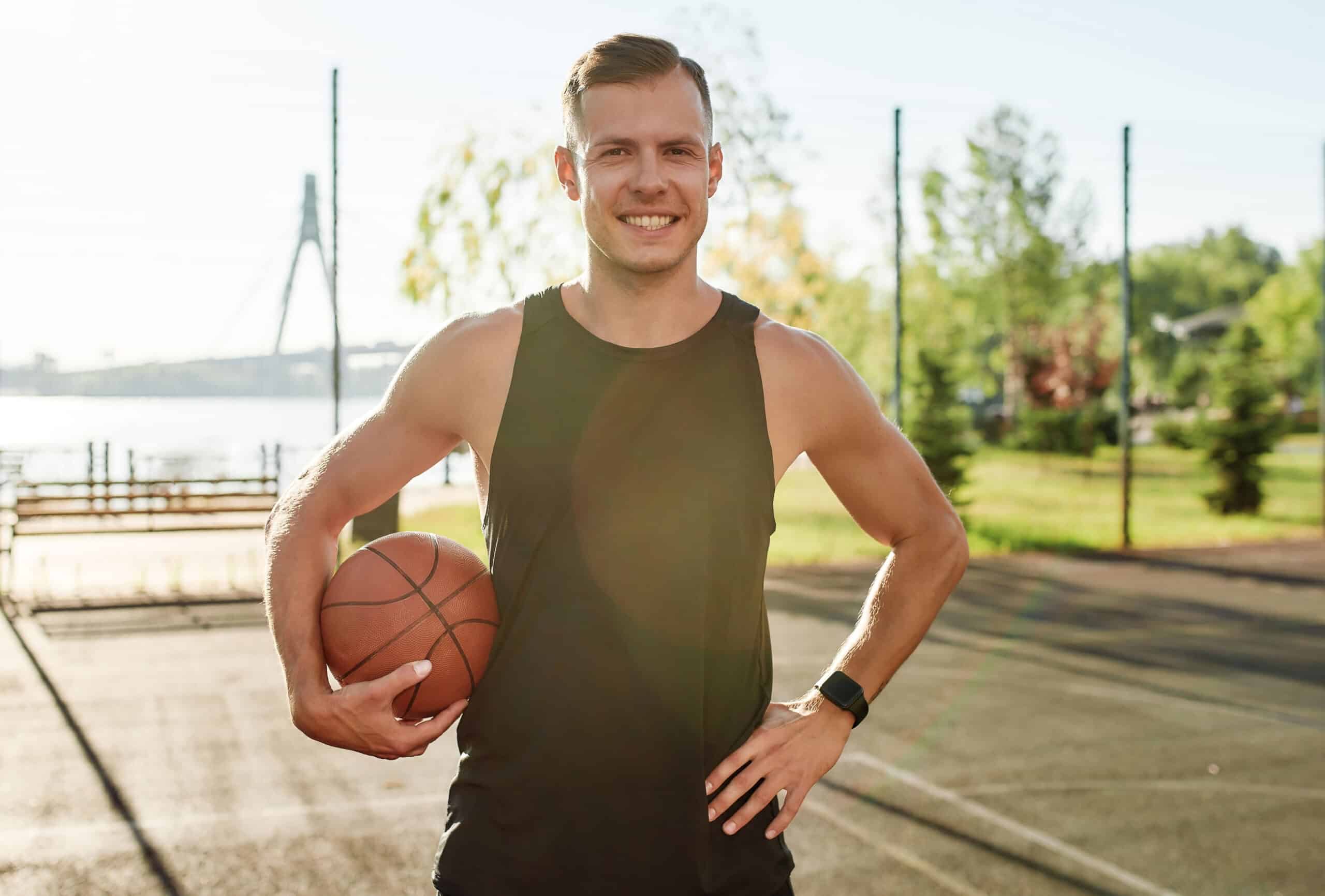 Man holding a basketball on a sunny outdoor court, emphasizing the importance of dental protection in sports.