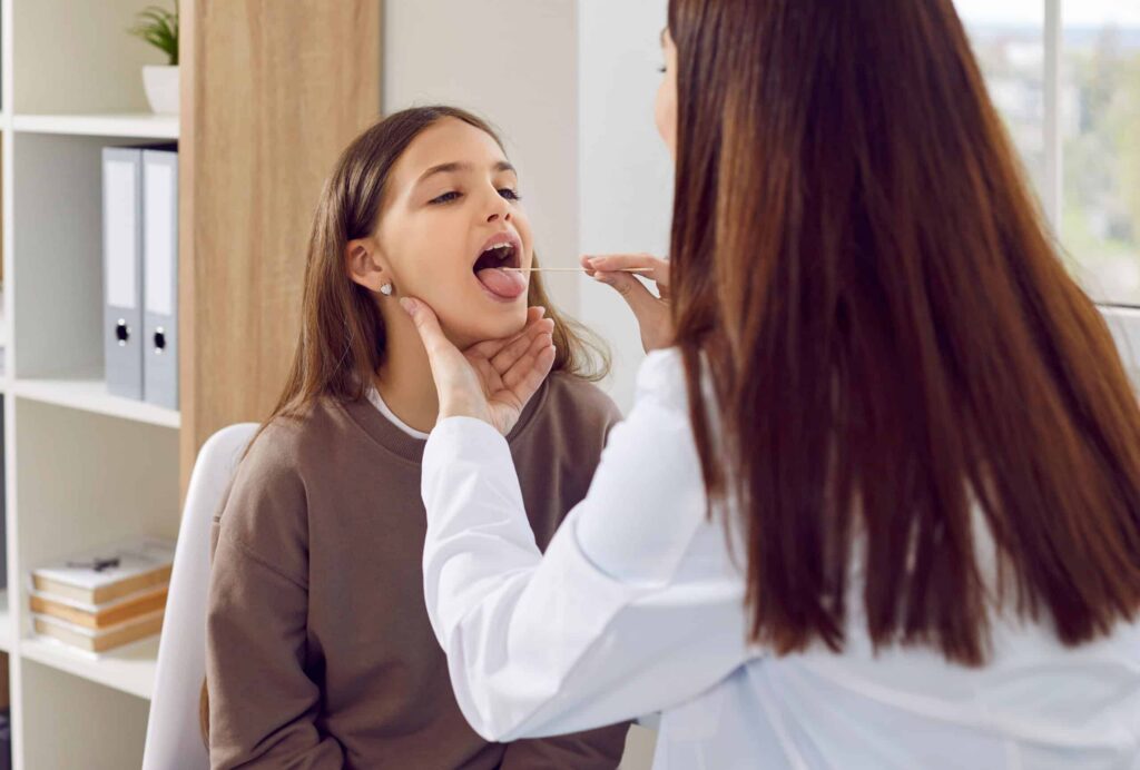 Young girl having her throat examined by a dentist, highlighting the importance of saliva in oral health and dental care.