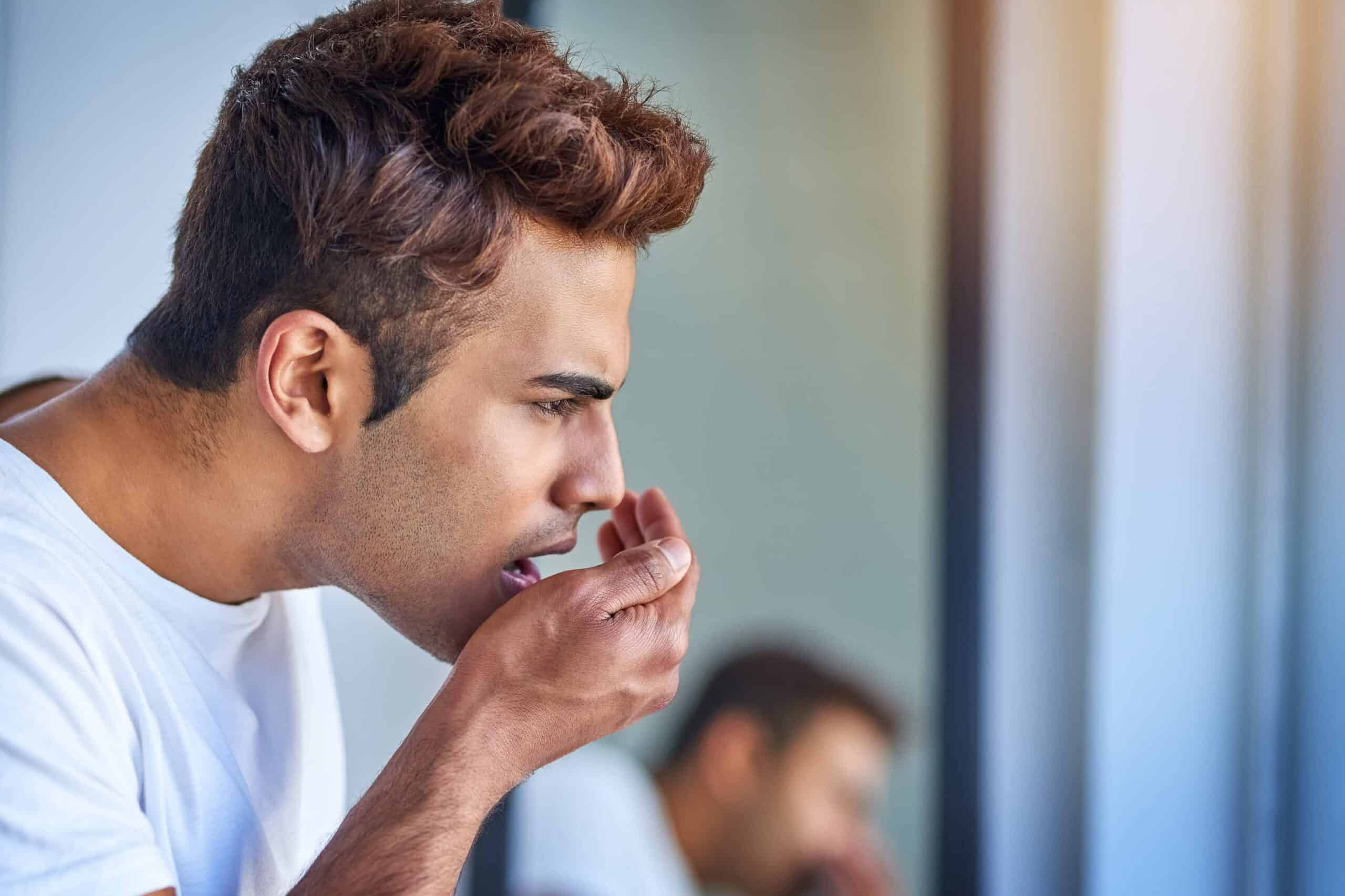 Man checking for bad breath while looking in a mirror, emphasizing oral health and hygiene.