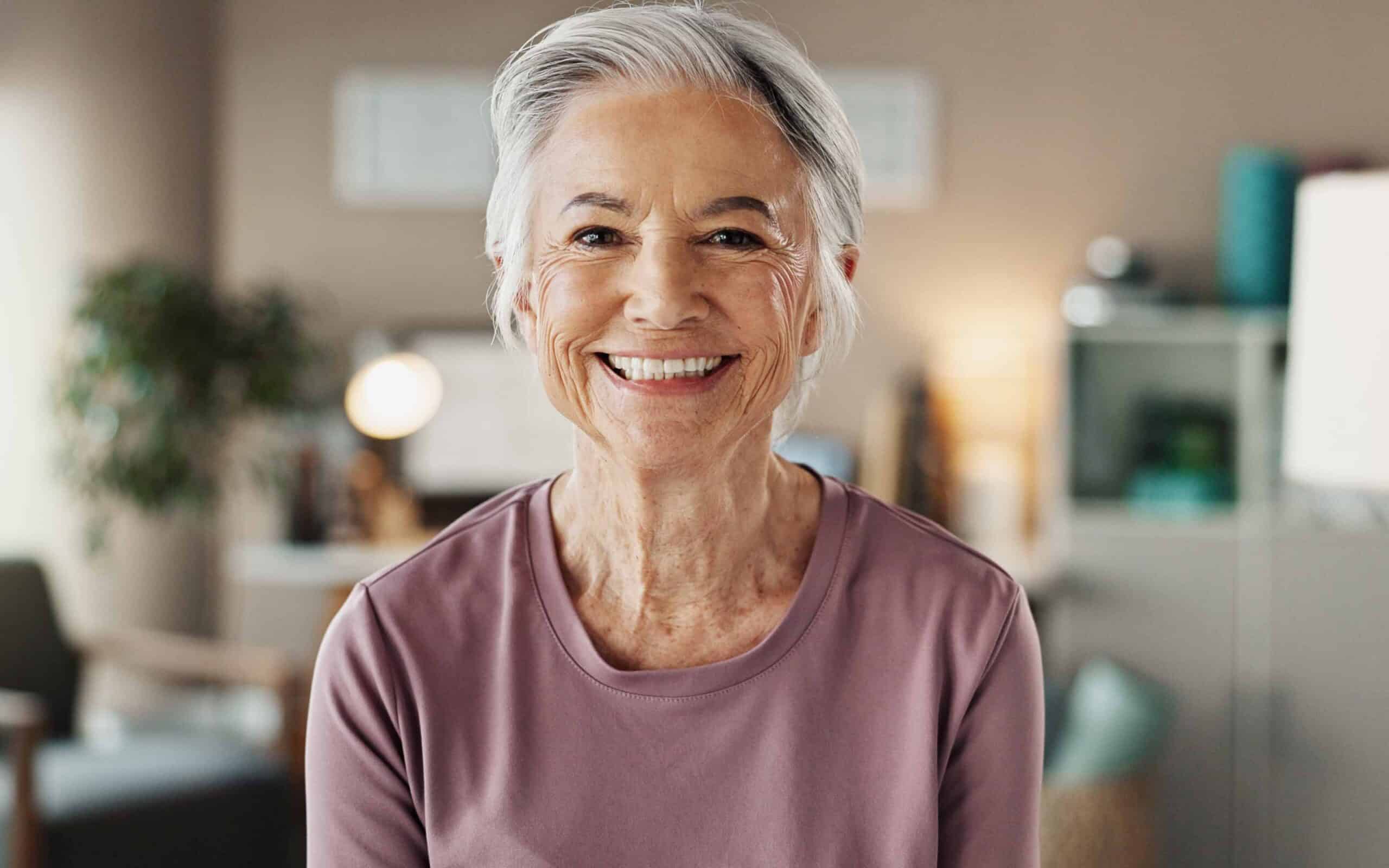 Smiling older woman in a cozy indoor setting, highlighting modern dental care and comfort in dentures.