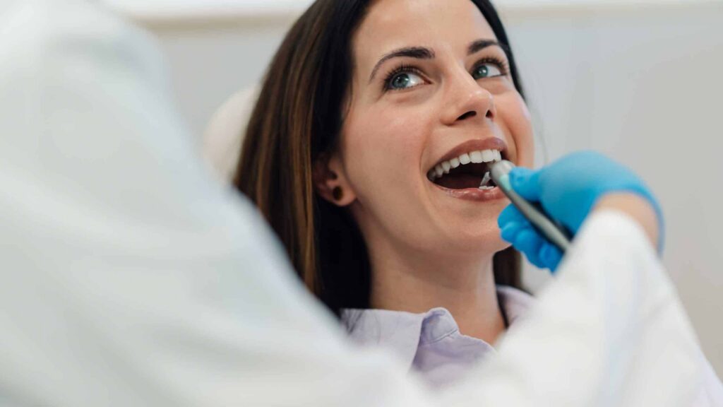 Woman smiling in dental chair during checkup, dentist examining teeth, emphasizing importance of regular dental visits and preventive care.