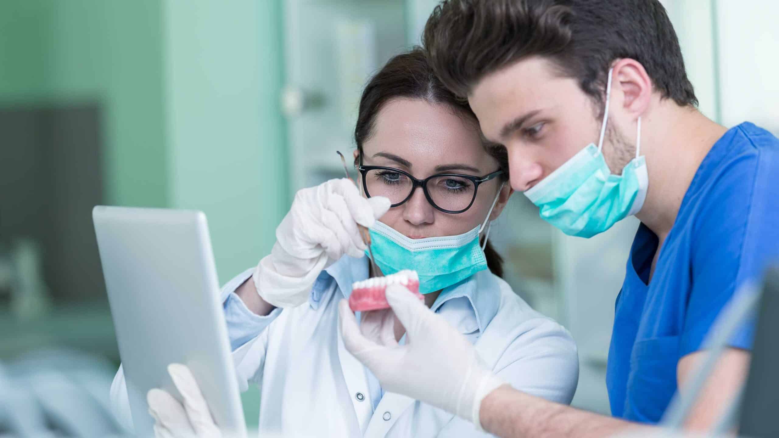 Dental professional demonstrating dental model techniques to student in clinical setting.