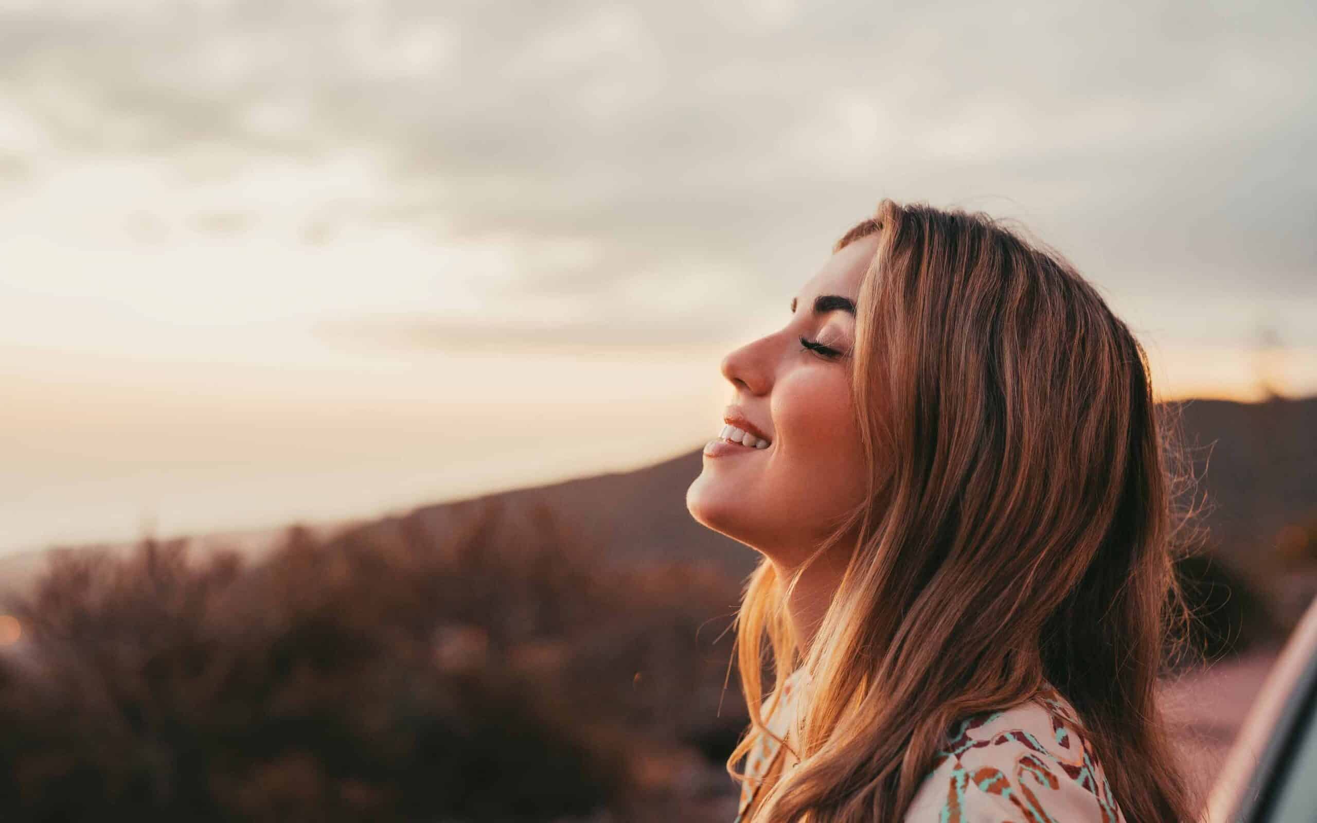 Young woman smiling outdoors, enjoying the sunset, reflecting on the impact of seasonal changes on oral health in Arizona.