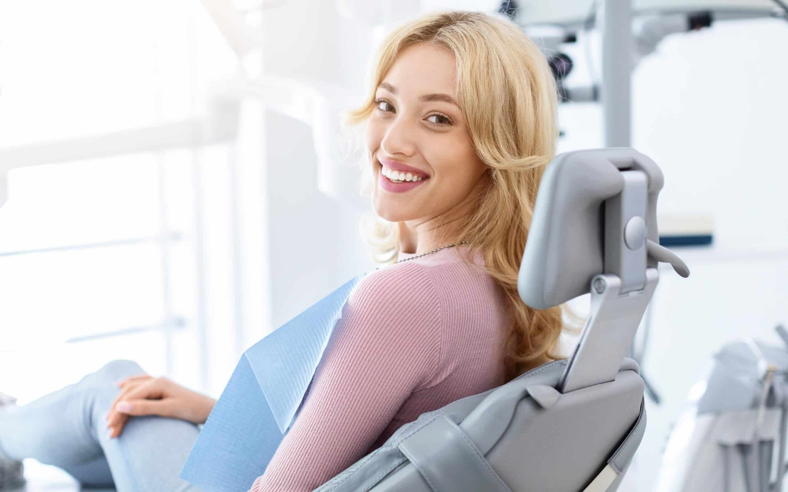 Smiling woman in dental chair wearing blue bib, illustrating modern dental care and patient comfort in a dental office setting.