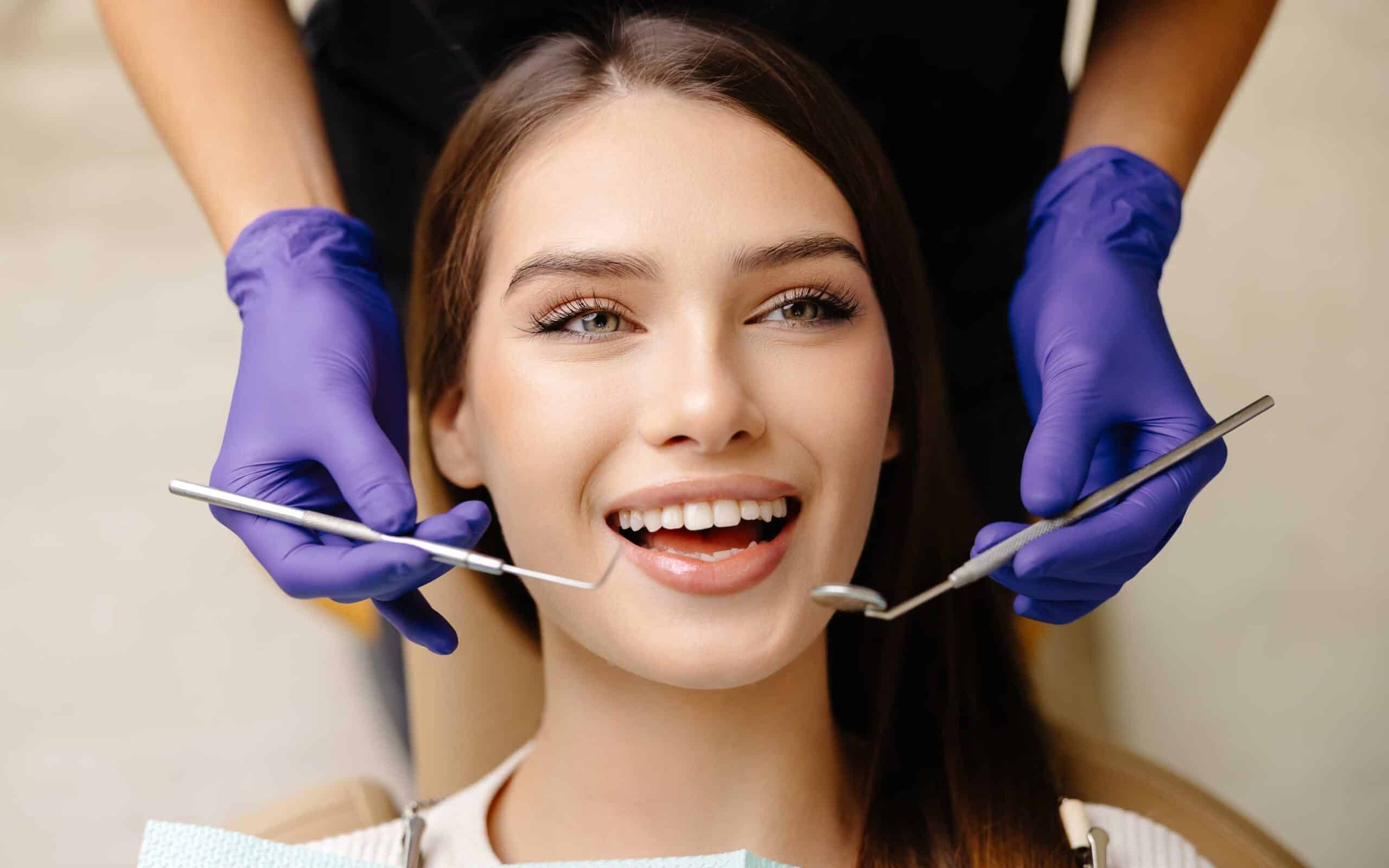 Woman smiling in dental chair during routine checkup, dental tools in use, emphasizing preventive care and affordability in dental services.