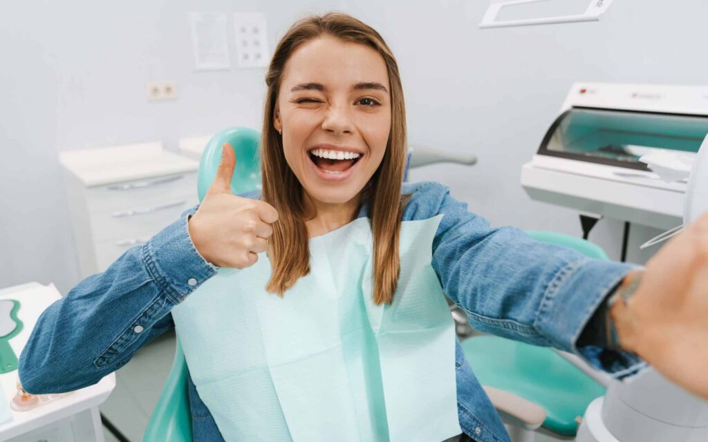 Smiling young woman in a dental chair giving a thumbs up, showcasing a positive dental experience at a full-service dental office.