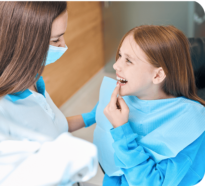 Child smiling and pointing to her teeth during a dental check-up with a dentist wearing a mask, emphasizing gentle care for children's dental health at Smith Dentalworks.