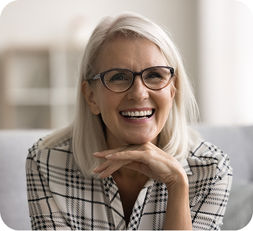 Smiling older woman with glasses showcasing a natural smile, representing confidence and satisfaction after receiving dental treatments, relevant to implant-supported dentures at Smith Dentalworks.