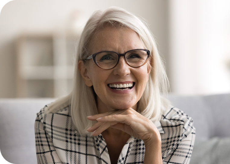 Smiling older woman with glasses showcasing a confident smile, representing the positive outcomes of dental treatments like implant-supported dentures.