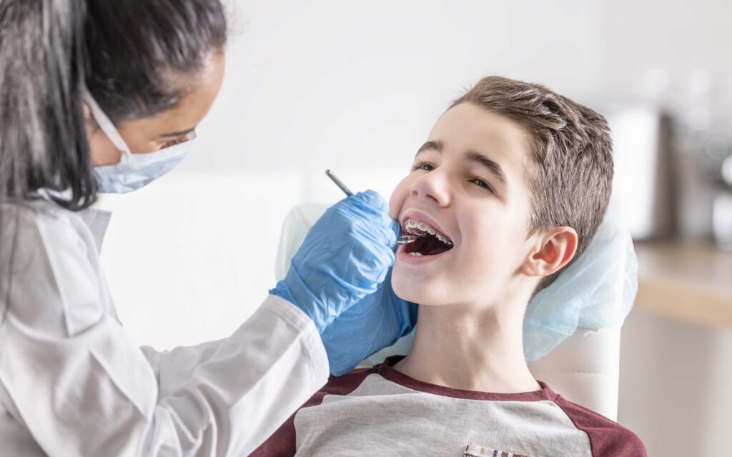 Dentist performing a back-to-school dental checkup on a child, examining his teeth during a routine oral health visit.